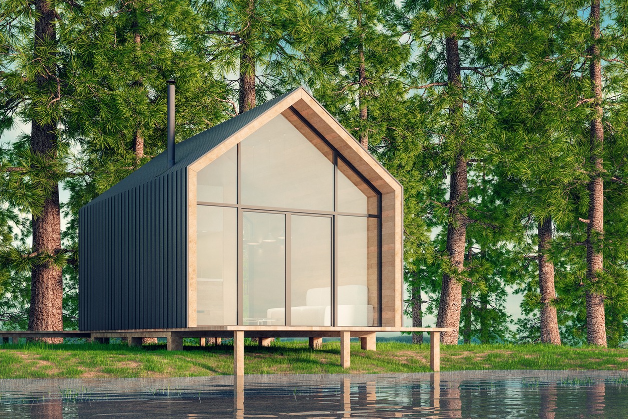 Wooden secluded house made of planks in a Scandinavian modern style with large Windows overlooking the lake, a fireplace at sunset against the background of a coniferous green forest. 3D illustration