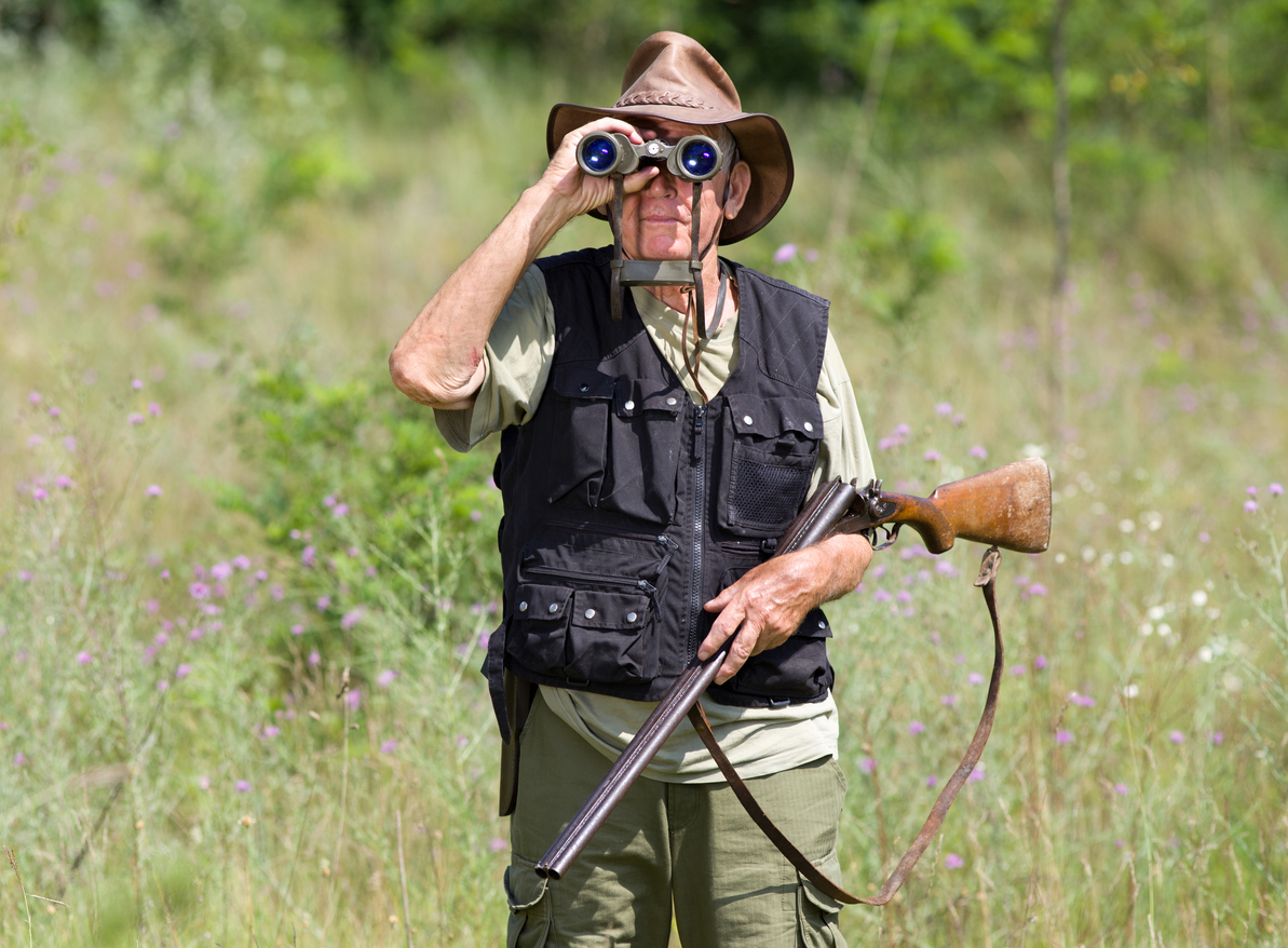 Senior hunter with shotgun looking through binoculars