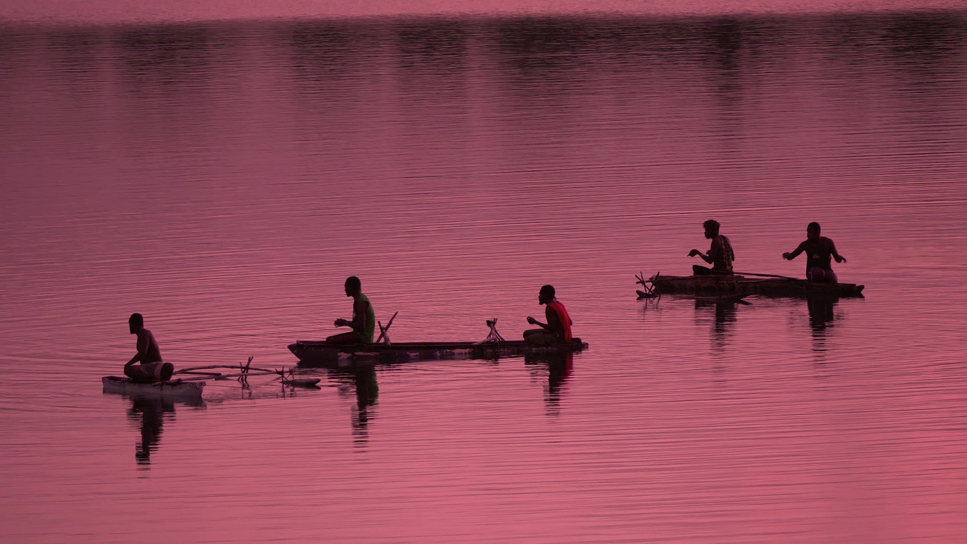 SILHOUETTE Unrecognizable local fishermen fishing in small boats at pink sunrise
