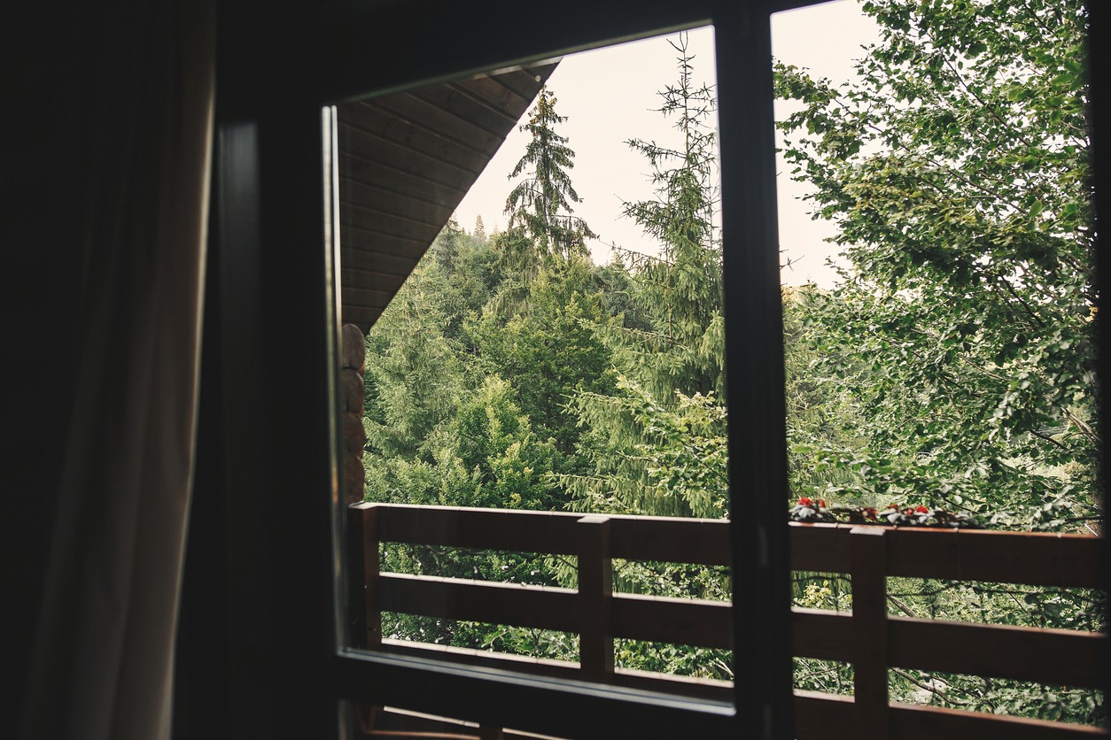 View from wooden cabin window on trees, woods and mountains. Space for text. Travel and vacations. Relaxing in log in forest