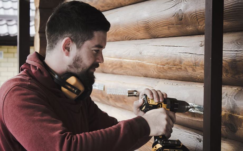 man using a drill on a wooden house