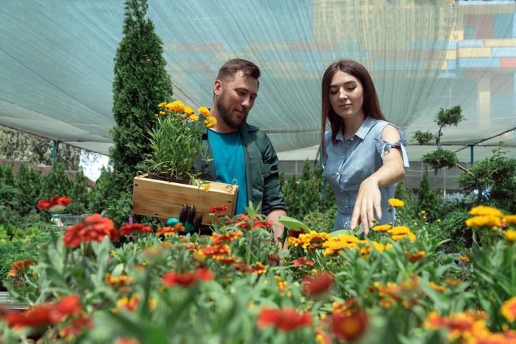 Worker helping female customer to buy flowers in garden center
