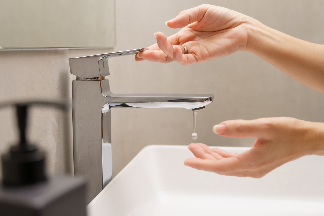 A woman’s hand turn on faucet with a drop of water dripping into hand